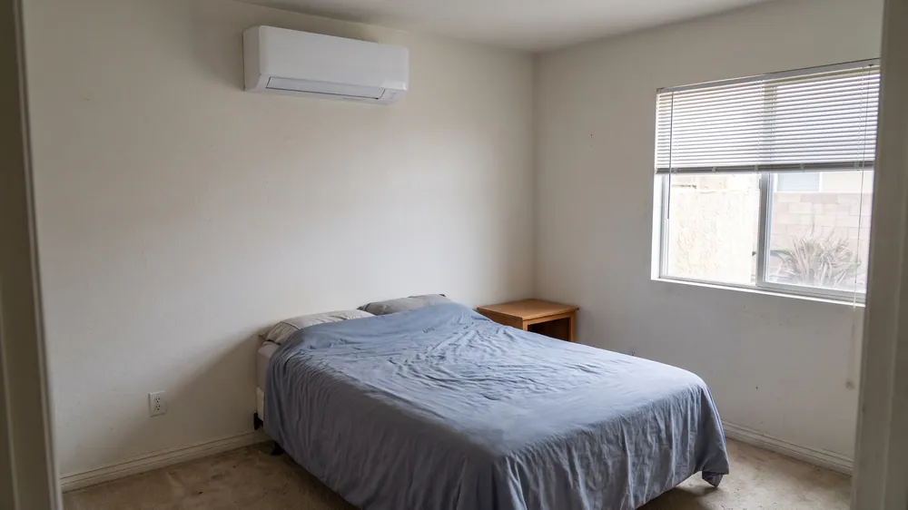 Indoor mini-split above a bed with a blue blanket.